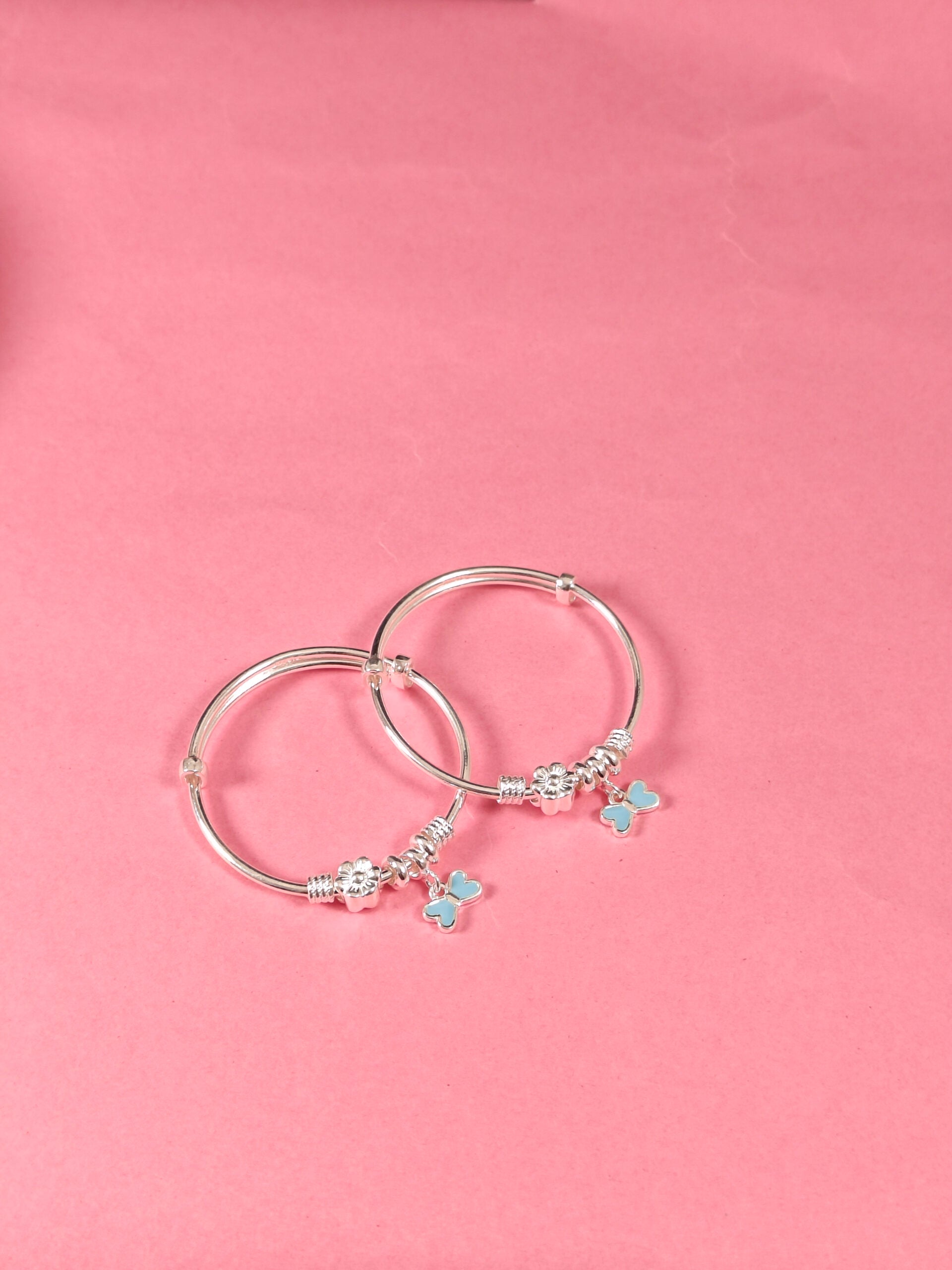 Silver hoop earrings with butterfly charms on a pink background